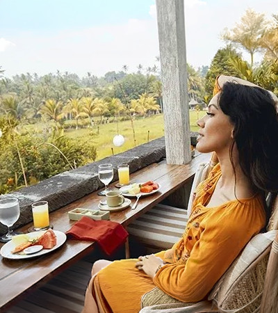 A woman sitting at a breakfast table on a balcony overlooking a verdant landscape