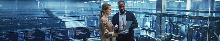 Two individuals standing in front of a server room, surrounded by rows of servers and blinking lights.