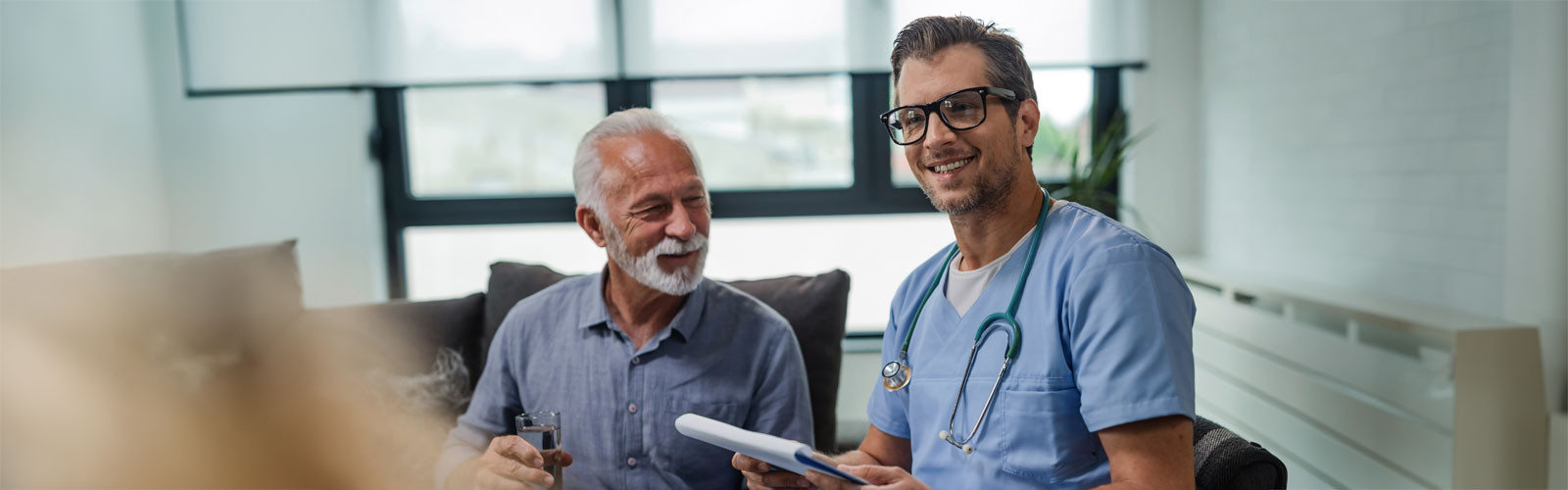 A male doctor sitting with an old patient in a hospital