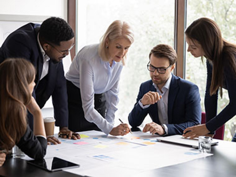 An office meeting with several colleagues looking at a number of pages on the table