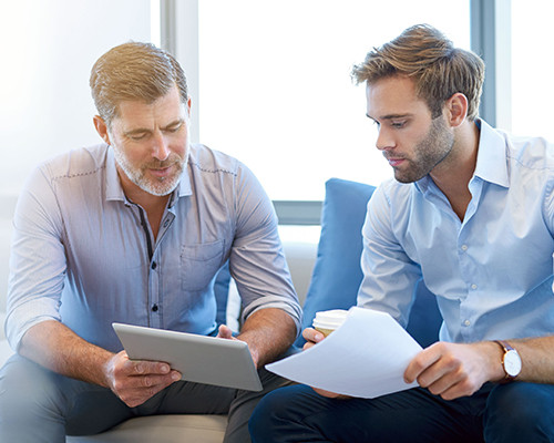 a man holing a tab is discussing with a man holding a paper