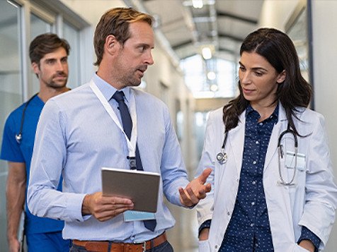 A doctor having a conversation with a man holding a tablet, while they are walking