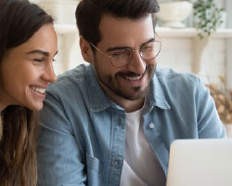 Un homme et une femme regardant un écran d'ordinateur portable, l'homme porte une chemise en jean et tous deux sourient.