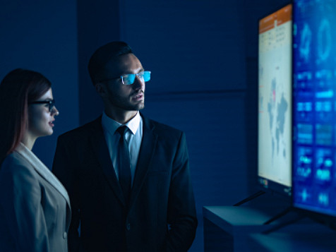 a man and a woman looking at the world map with statistics on a computer screen.