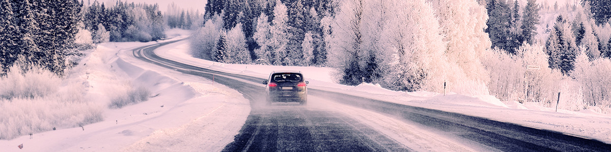 A car driving by snow-covered trees on both sides of the road in winter