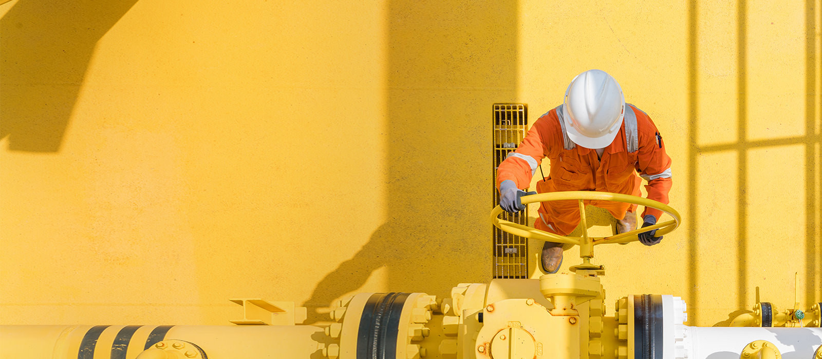 A worker in a high-visibility safety dress and white helmet operating a release valve