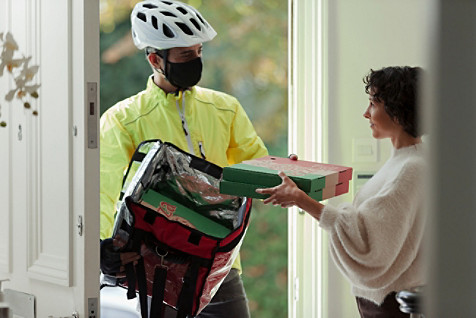 Une femme portant un masque réceptionnant à une porte d'entrée une pizza livrée par un coursier