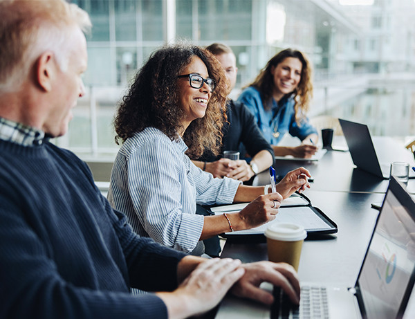 A group of diverse individuals seated at a table, each using a laptop for collaborative work or discussion