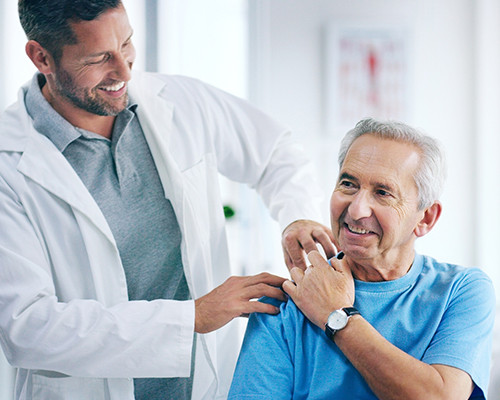 A man in a white jacket massaging an elderly man's shoulder