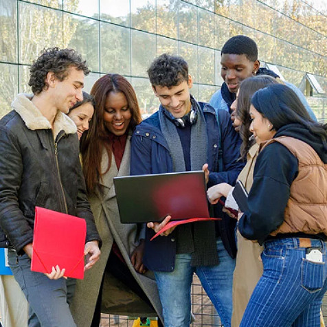 Vielfältige Gruppe junger Männer und Frauen steht um einen jungen Mann herum und schaut auf seinen Laptop