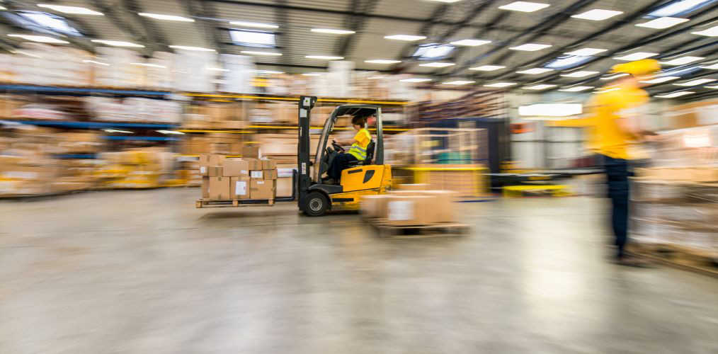 An employee driving a forklift truck with cargo in a warehouse 