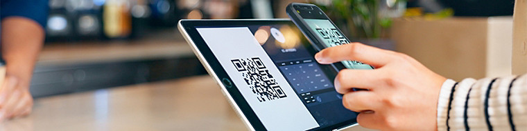 A person is holding a tablet displaying a QR code, ready to scan for information or access a digital resource.