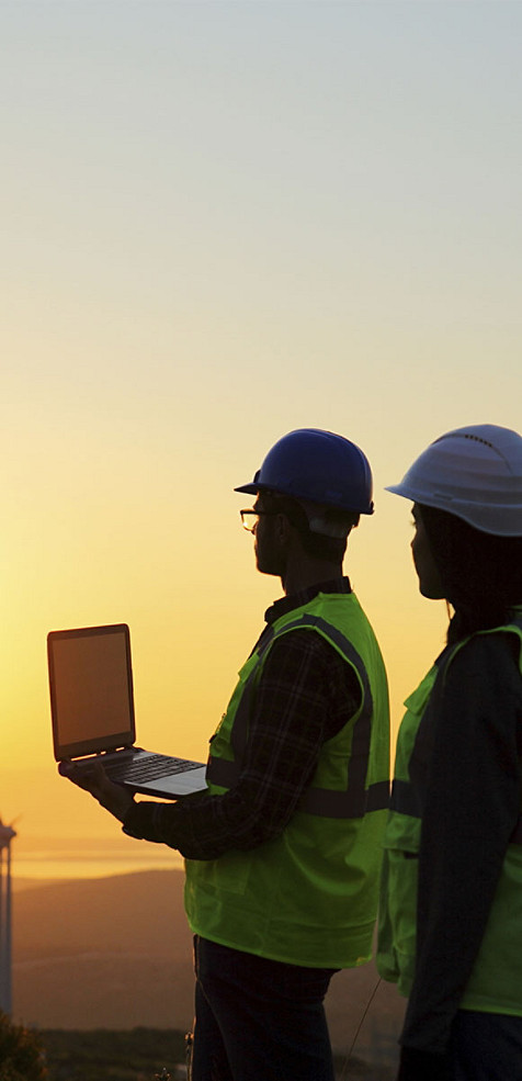 Two workers standing outdoors and looking at a laptop