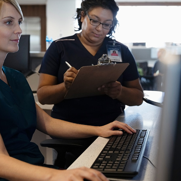 Two ladies at a computer; one sitting at keyboard; one standing with a clipboard