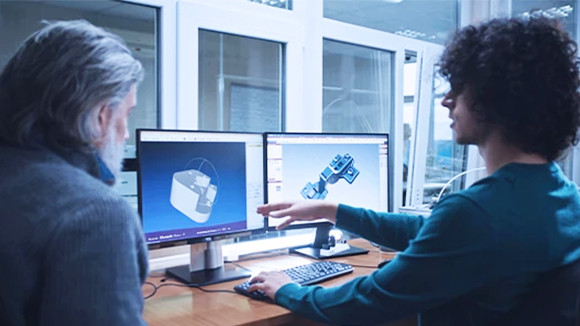 Two men looking at two monitors on a desk, displaying 3D models