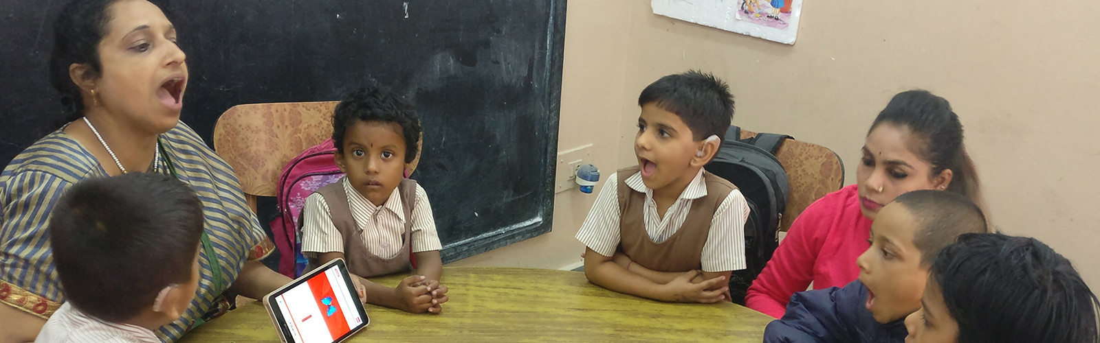 Students are sitting around the teacher and listening to her