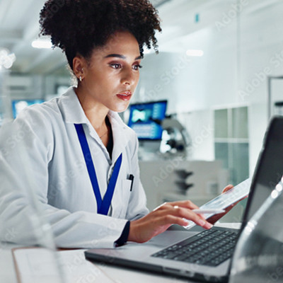 A lady wearing a white lab jacket, sitting at a desk and working on a laptop