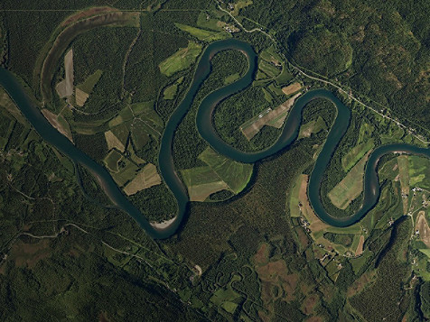 Aerial view of a winding river flowing through a lush green valley surrounded by hills and trees.