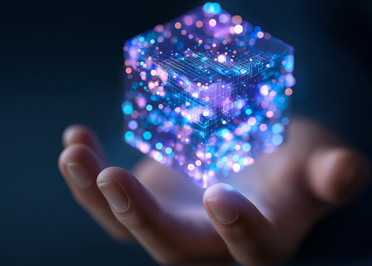 A cupped hand holding a glowing, translucent cube made of digital particles and grid lines in blue and purple, representing a modular, holographic data structure.