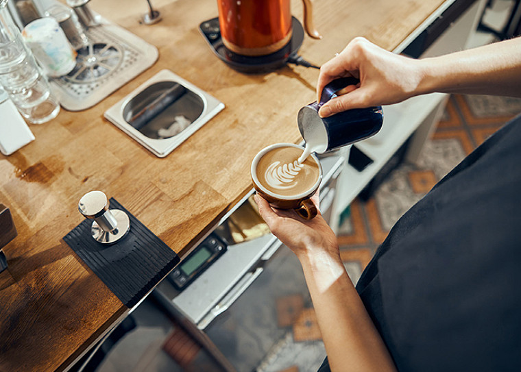 a top view of a barista pouring milk over coffee near a table