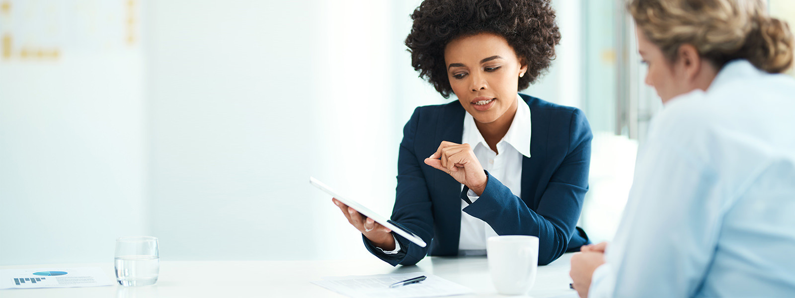 Two women colleagues in discussion while looking at a tablet.