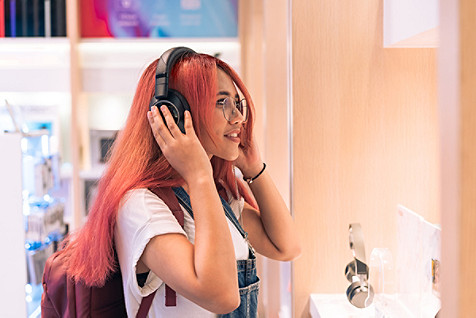 Asian social influencer woman trying on headphones inside retail store - Happy millennial diverse girl shopping and testing lifestyle music tech products - Technology, electronic and purchase concept