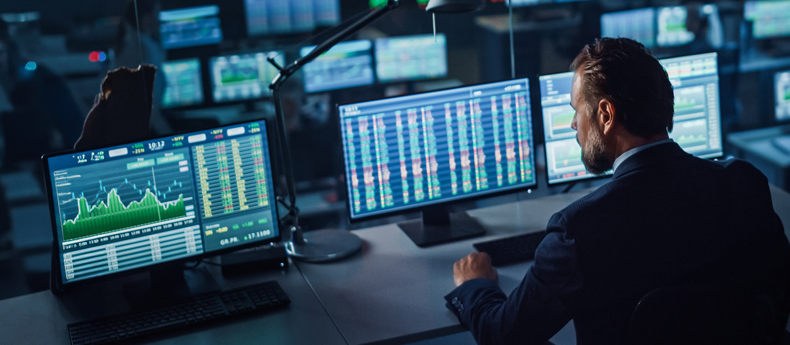 Trader at multiple monitors analyzing stock charts and financial data