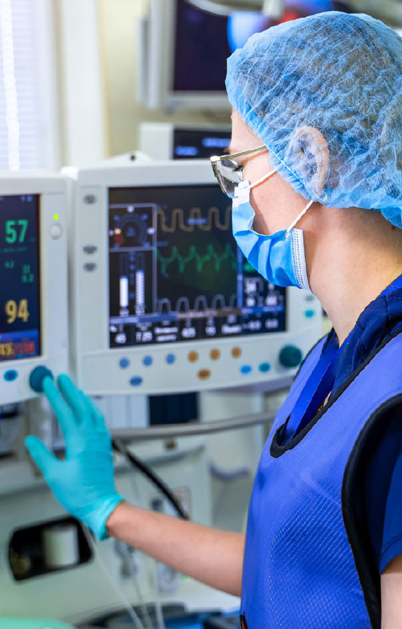 Healthcare worker with facemask and hairnet looking at monitor screen