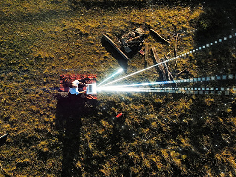 Luftaufnahme eines Traktors, der einen Laserstrahl aussendet, was fortschrittliche landwirtschaftliche Technologie auf dem Feld hervorhebt