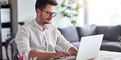 Mann sitzt vor dem Computer-Laptop an seinem Schreibtisch mit Dokumenten und Mobilgeräten