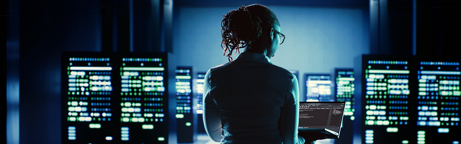 Kvinna i blå skjorta tittar på sin bärbara dator på ett skrivbord