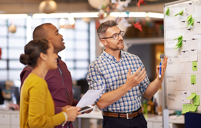 Three colleagues looking at a whiteboard having a discussion