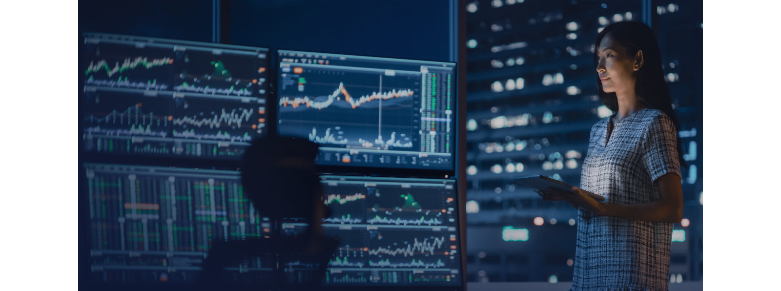 A woman looking at multiple screens showing data and graphs