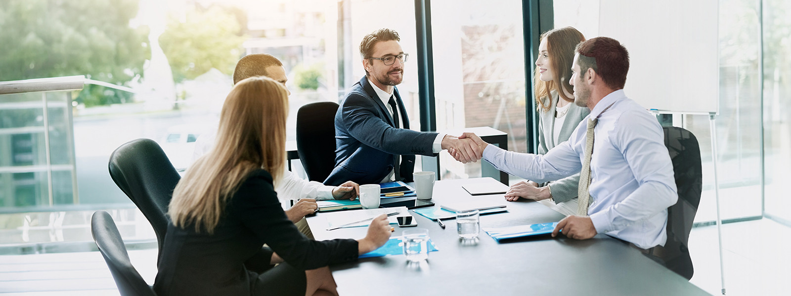 A group of professionals in a meeting room, shaking hands across the table