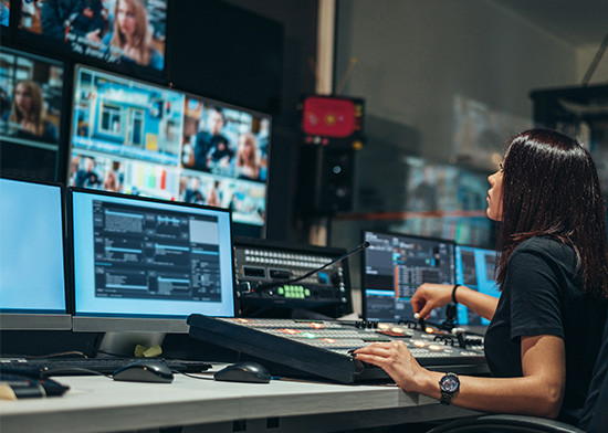 A woman seated at a desk, focused on multiple computer monitors displaying various applications and data.