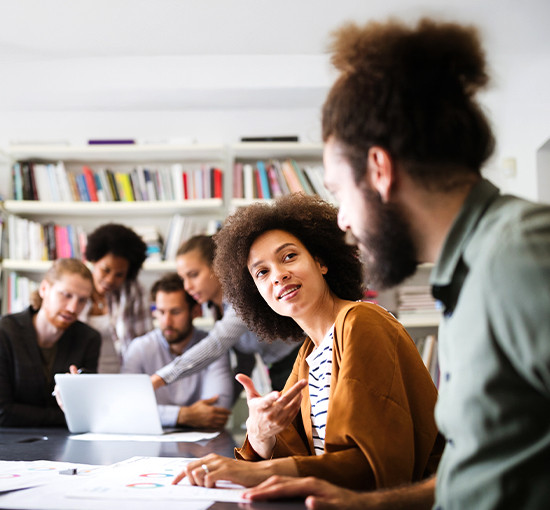 A diverse group of people seated around a table, each using laptops for a collaborative work session.