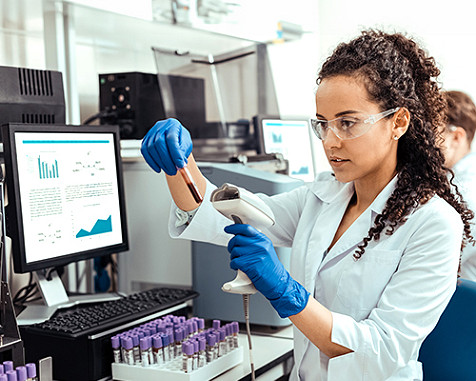 A woman examining a test tube sample in front of a monitor