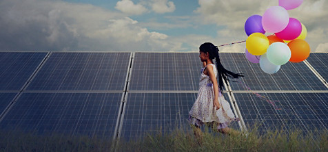 Una chica corriendo junto a un panel solar con un montón de globos en la mano