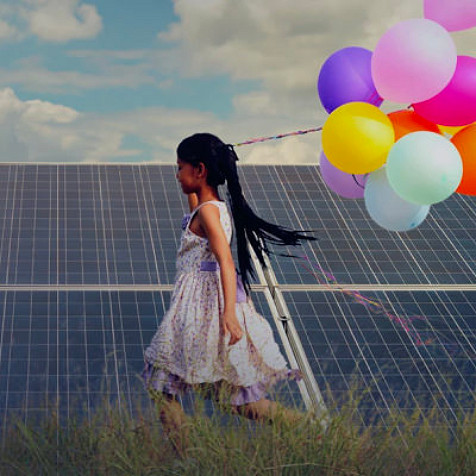 A girl running beside a solar grid holding a bunch of balloons in her hand
