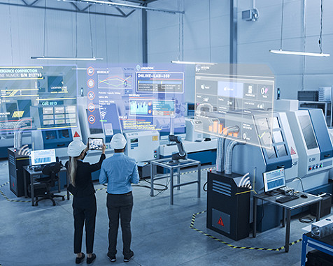 Man and woman in hard hats, back turned to us, standing in a tech room