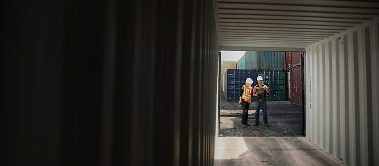 En vy från insidan av en container med två anställda som arbetar med en checklista