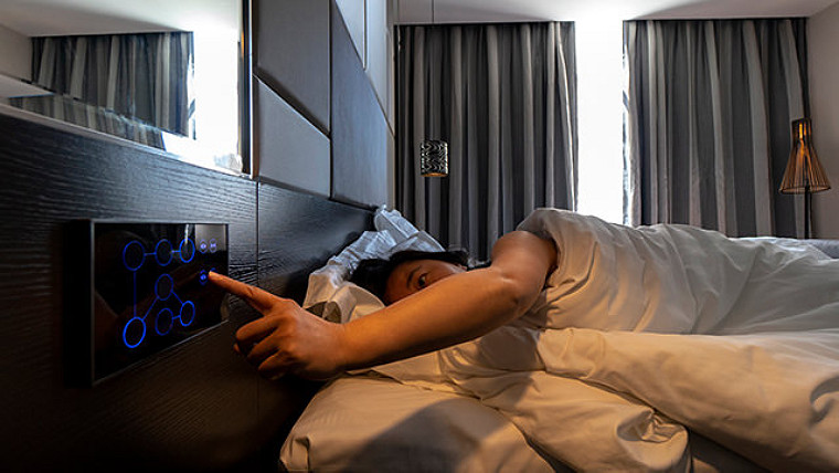 person lying on bed using adaptive digital equipment to control room settings.