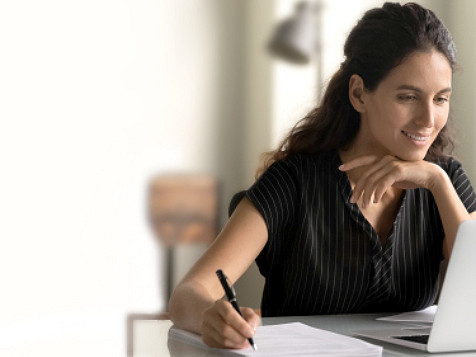 woman looking at a computer and writing notes