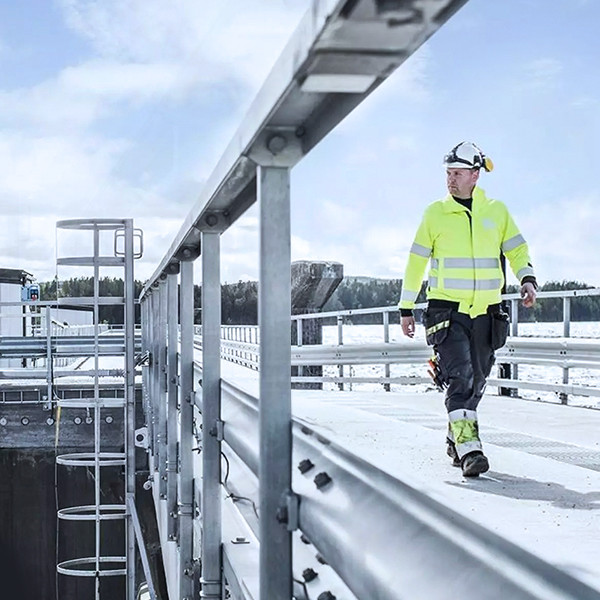 A worker  walking on a ramp, wearing a helmet and hazard jacket