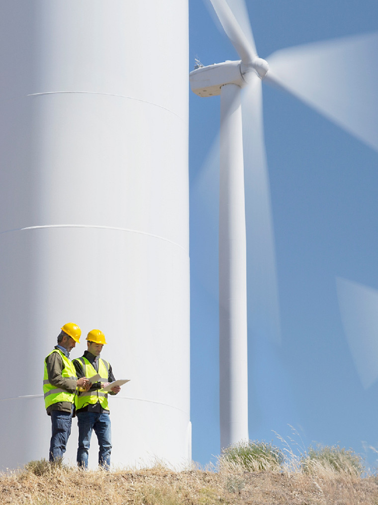 two workers standing beside a wind turbine