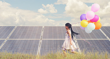 littel girl holding balloons in front of solar panels