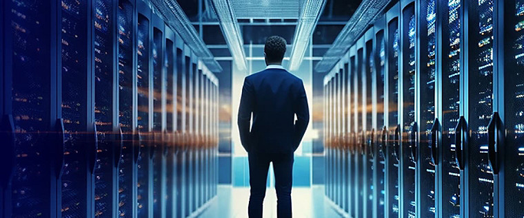 A man standing, with his back to the camera, in  a server room