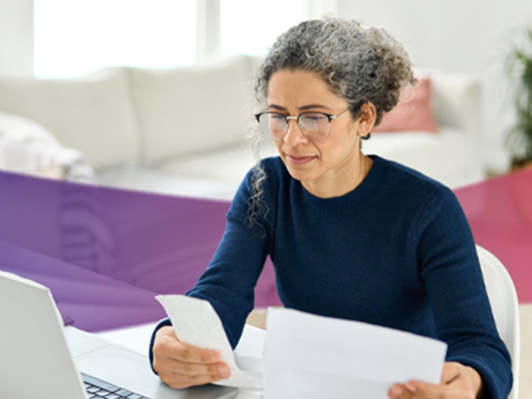 woman looking at laptop and holding papers