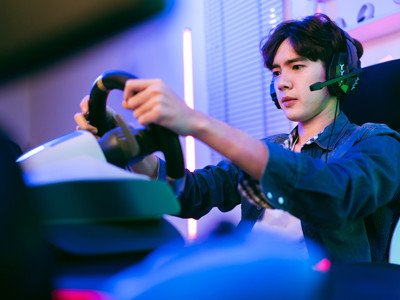 A man sitting at a gaming steering wheel while on a headset.