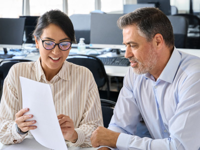 a woman office worker pointing to a document and explaining to a male colleague at work